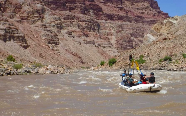 A group of students in a raft raise their paddles into the air. 